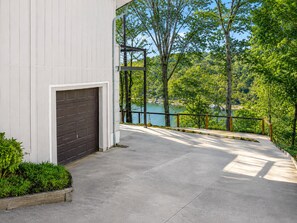 A building with a garage door, a concrete pathway, and a view of a lake surrounded by trees.