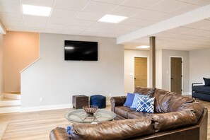 A modern living room with a leather sofa, a glass coffee table, and a flat-screen TV mounted on the wall.