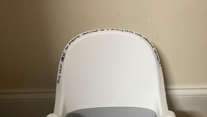 A high chair with a tray and two divided plates, one teal and one orange, against a plain wall.