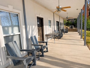 A covered outdoor seating area with tables and chairs, a ceiling fan, and a building with windows and doors. - The Gathering Place: Big Lakehouse/Covered Dock/Fiber/Tankless WH/Game RM/EV CHG (Cullman)