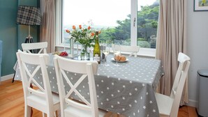 Un comedor con una mesa dispuesta para dos personas, una ventana con cortinas y vistas al exterior con vegetación.