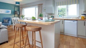 Una cocina moderna con una isla central, taburetes de bar, lavavajillas y un área de comedor con sofá y sillas.