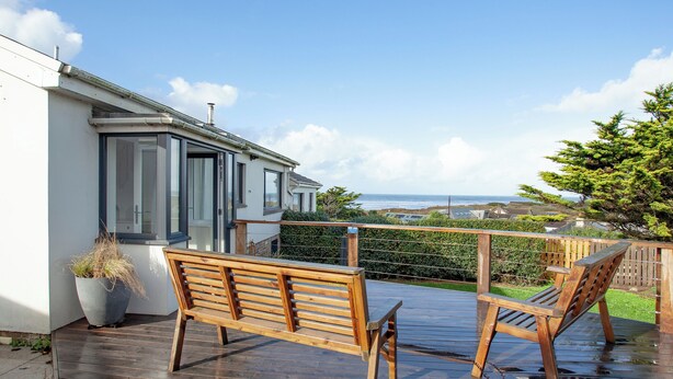 Una terraza de madera con dos bancos que da a una zona residencial y al mar.
