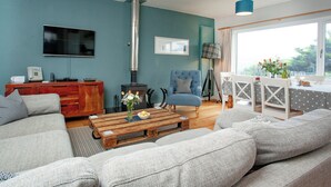 Una sala de estar con un sofá, una mesa de centro, un sillón azul, un televisor, una chimenea y un comedor con una mesa y sillas.