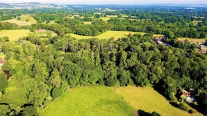 Une vue aérienne d’un paysage rural, avec des champs verdoyants vallonnés, des arbres dispersés et quelques bâtiments.