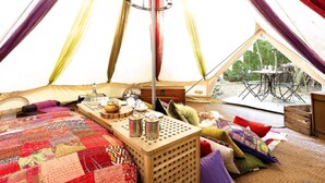 L’intérieur d’une tente accueillante, avec un lit, une table où est disposé un service à thé, et une vue sur l’extérieur.