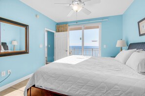 Quarto com cama grande, ventilador de teto, porta para uma varanda e vista para o mar.
