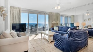 A spacious living room with a large window offering a view of the ocean, a ceiling fan, and a flat-screen TV. - 🌴Gulf Views~Steps2Beach~Pool~Beach~Hot Tub~3BR Island Princess 315🌴 (Fort Walton Beach)