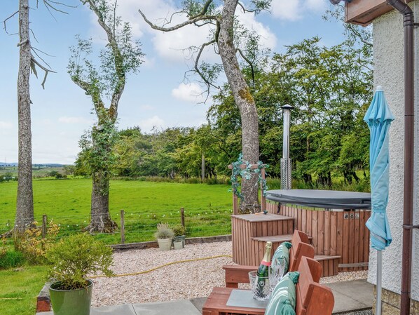 A patio with outdoor seating, a hot tub, and a view of a green field.