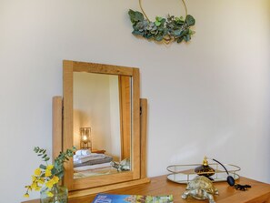 En spegel med träram som speglar ett rum med en säng, en lampa och en liten skulptur av en sköldpadda på ett träbord.