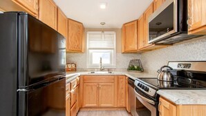 Une cuisine avec des meubles de rangement en bois, un réfrigérateur noir, une cuisinière et un évier.