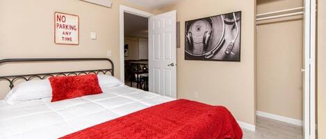 A bedroom with a bed, a red blanket, a 'NO PARKING ANY TIME' sign, and a door leading to a bathroom.