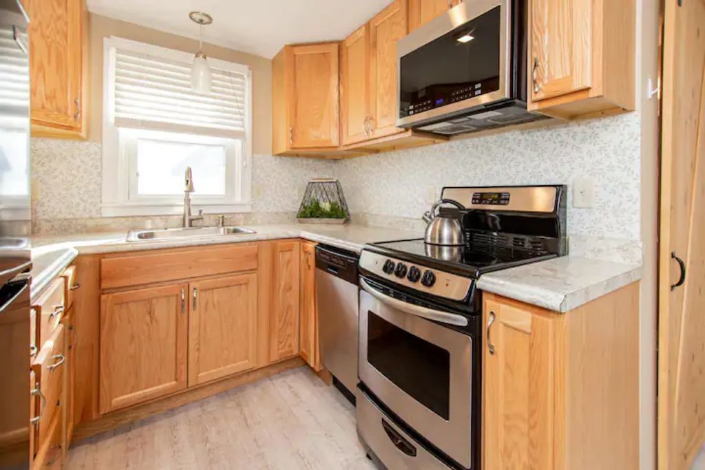 Una cocina con armarios de madera, estufa de acero inoxidable, microondas y un lavabo.