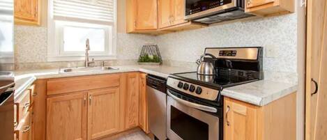 A kitchen with wooden cabinets, a stainless steel stove, a microwave, and a sink.