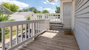 Une terrasse en bois avec une balustrade blanche, qui mène à un espace porche abrité.