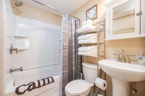 Un bagno con una vasca, una tenda da doccia, un water, un lavandino e un portascopevoli con asciugamani piegati con cura.