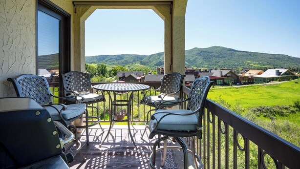 A balcony with outdoor seating, a view of green hills, and a clear sky.
