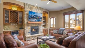 A cozy living room with a stone fireplace, leather sofas, and a large TV mounted on the wall.