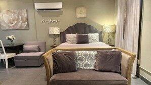 Une chambre à coucher comprenant un lit, une chaise longue, une table de chevet avec des lampes et un climatiseur fixé au mur.