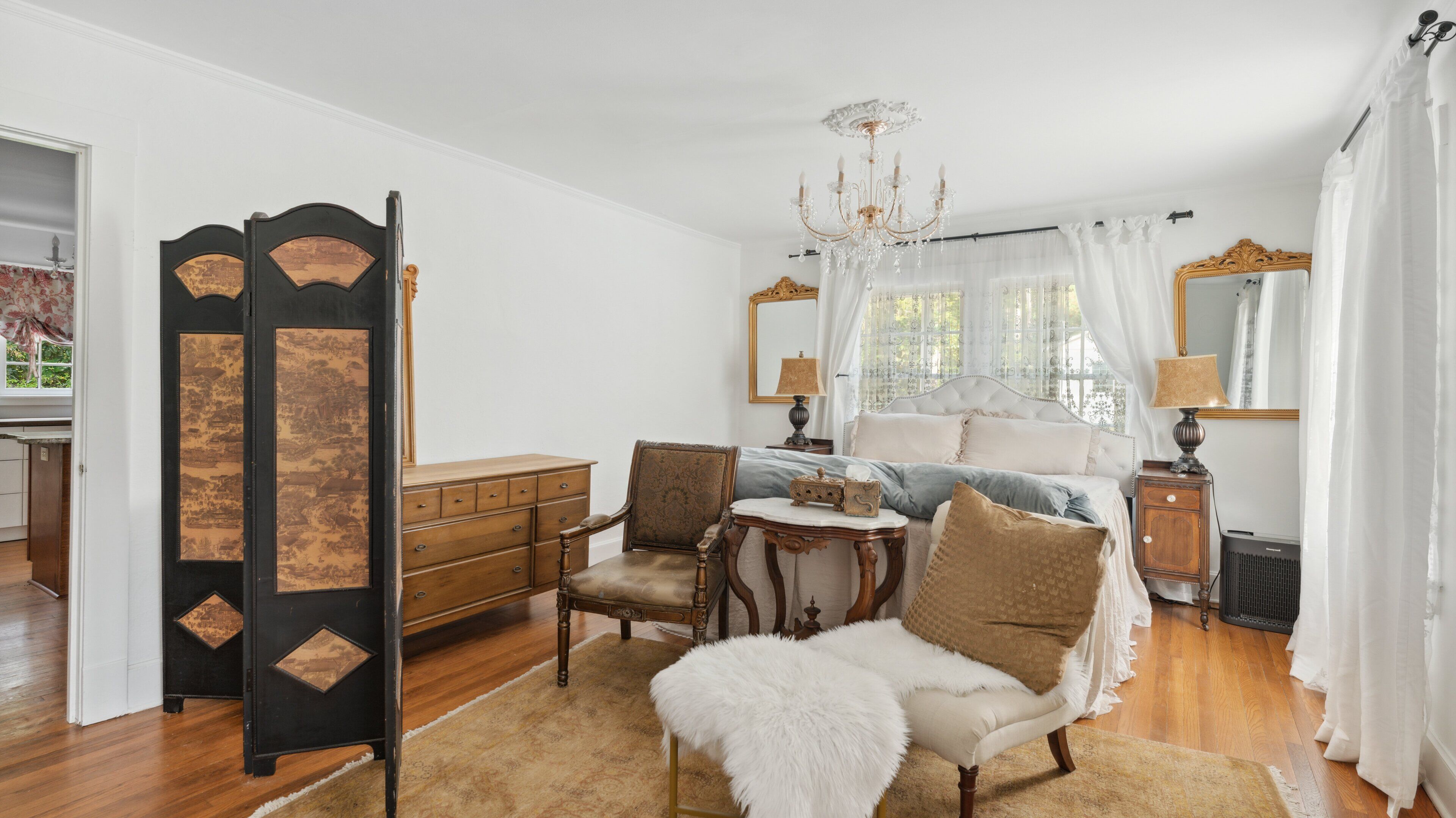 A bedroom with a bed, a dresser, a chair, a small table, and a mirror.