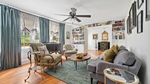 Een woonkamer met een bank, fauteuils, een salontafel en een boekenplank vol boeken.