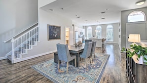 A spacious living area with a dining table, chairs, and a patterned rug. A staircase with white railings leads to another level. - 3-Story Houston Townhome: 1 Mi to Minute Maid Park (Houston)