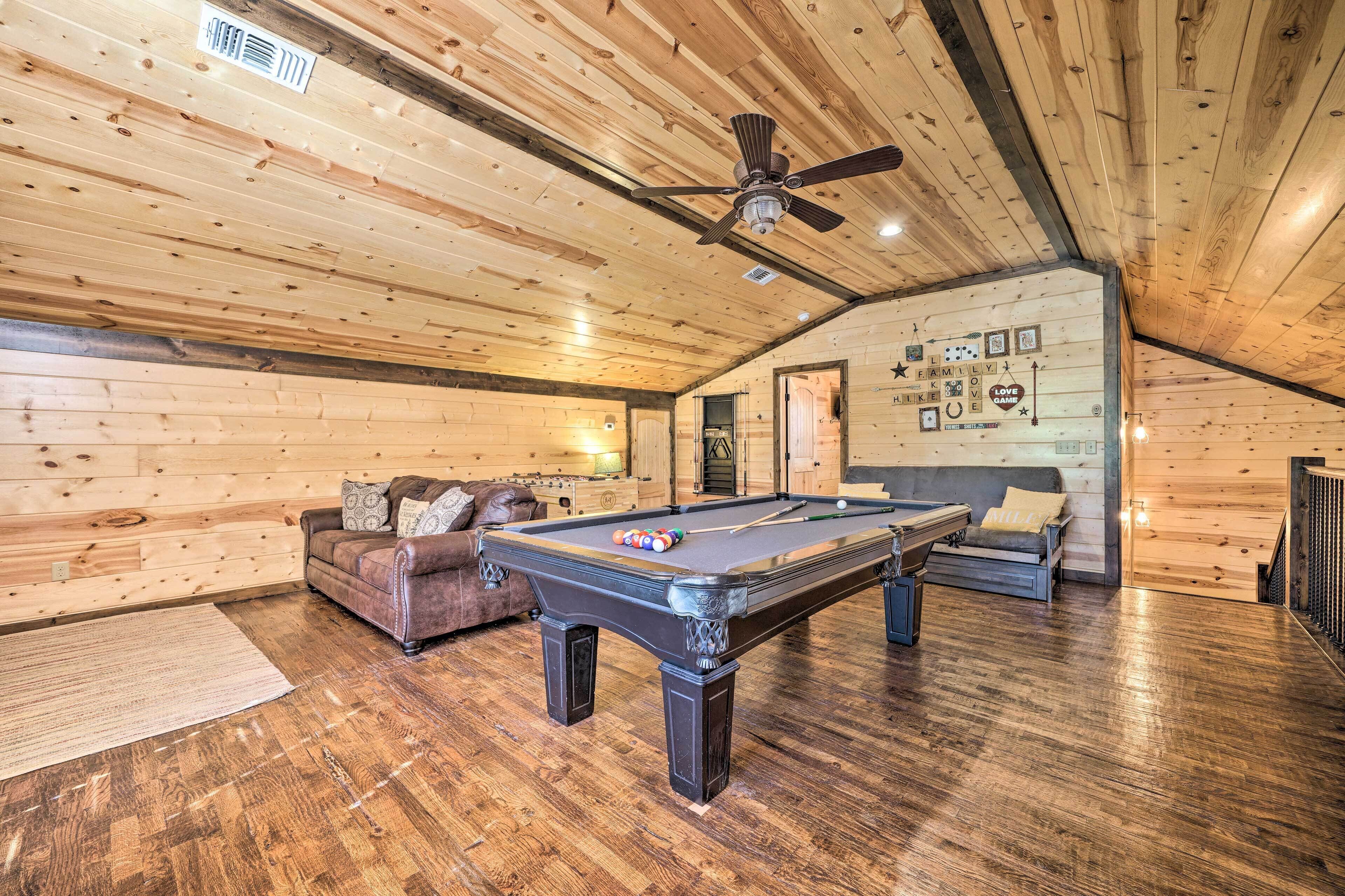 A wooden interior with a pool table, leather sofa, and a ceiling fan.