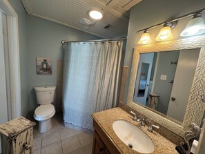 A bathroom with a toilet, shower curtain, sink, and mirror. - Paradise PRN (gulf shores)