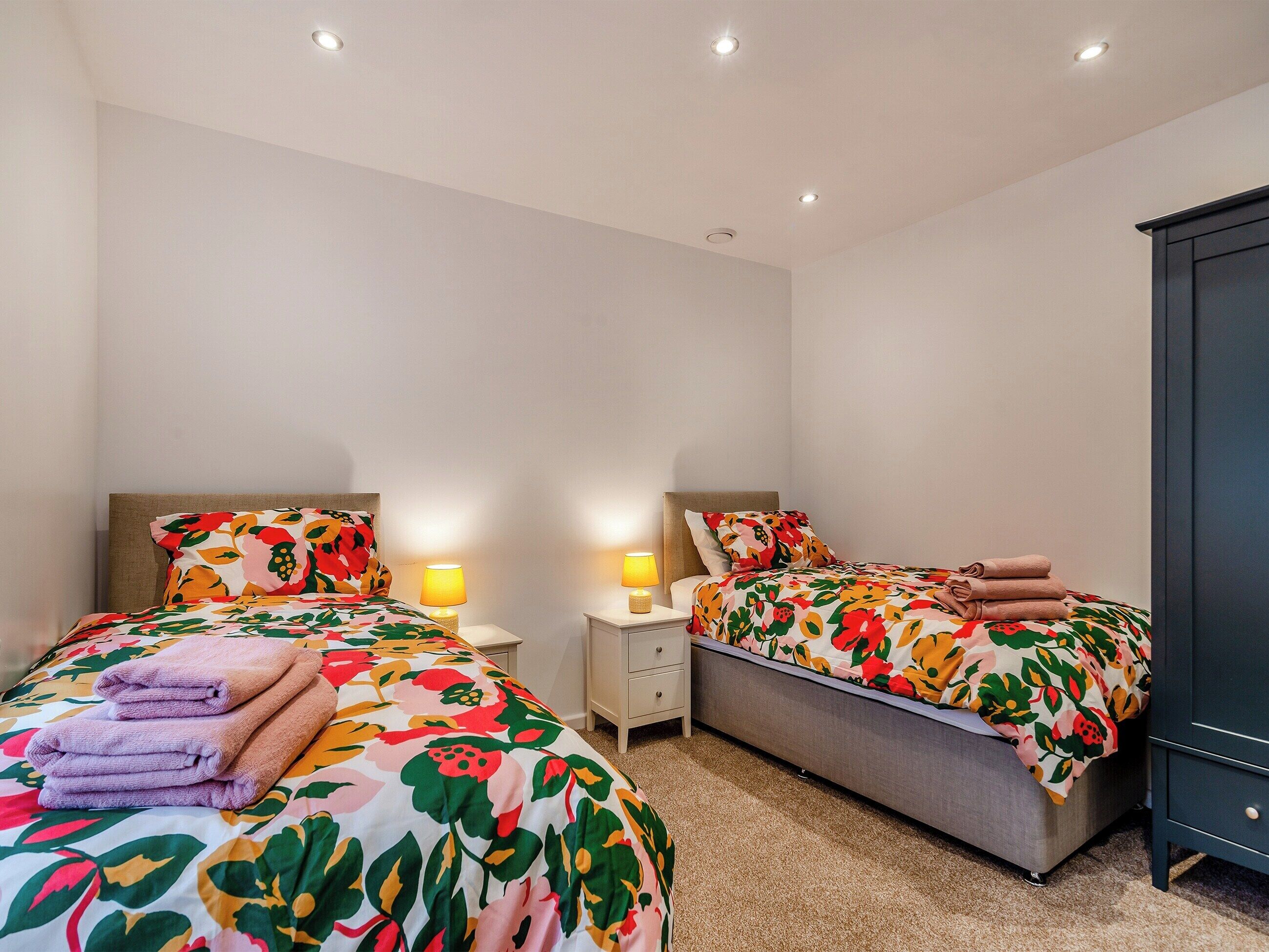 Une chambre d’hôtel avec deux lits, chacun agrémenté d’une literie à motifs floraux et d’une table de chevet avec une lampe.