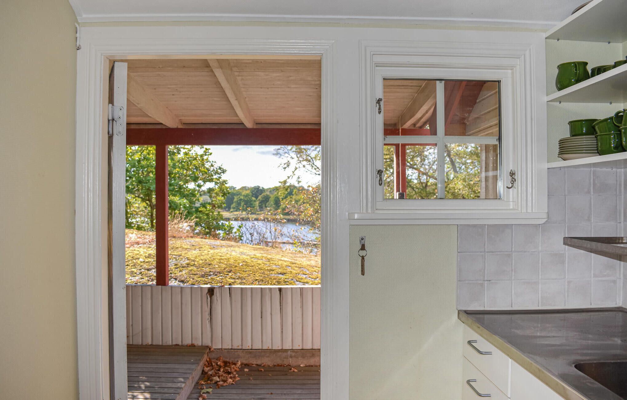 Une cuisine avec vue sur un lac, une terrasse en bois et une fenêtre donnant sur les arbres.