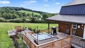 A wooden deck with a hot tub and barbecue grill, overlooking a grassy field and hills. - Ridge top cabin with hot tub and movie theater (Logan)