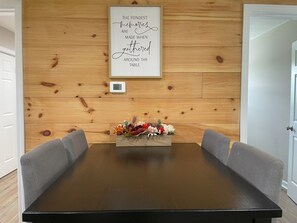 Pared de paneles de madera con una cita enmarcada, un termostato y un arreglo floral sobre una mesa.