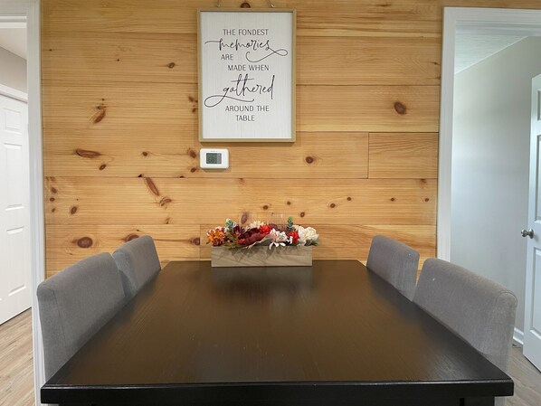 Un mur lambrissé en bois, orné d’un cadre contenant une citation, d’un thermostat et d’un arrangement floral posé sur une table.