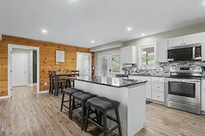 A modern kitchen with white cabinets, stainless steel appliances, and a wooden accent wall. - Ridge top cabin with hot tub and movie theater (Logan)