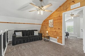 A room with a black sofa, a small side table, a ceiling fan, and a wooden wall.