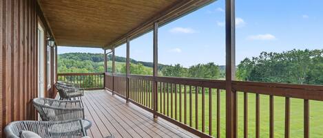 A wooden deck with a railing, wicker chairs, and a view of a green landscape.