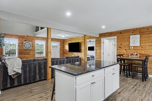 A modern kitchen with wooden paneling, a central island, and a dining area with a table and chairs. - Ridge top cabin with hot tub and movie theater (Logan)