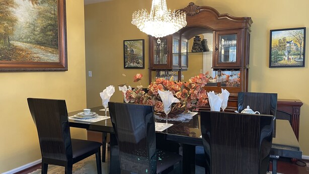 Un comedor con una mesa dispuesta para seis comensales, rodeada de sillas oscuras, un candelabro y cuadros en las paredes.