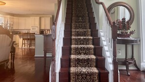 Una escalera con alfombra estampada, barandillas de madera y un espejo decorativo.
