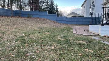 Un área con césped, una valla azul, un sendero y un edificio con fachada blanca.