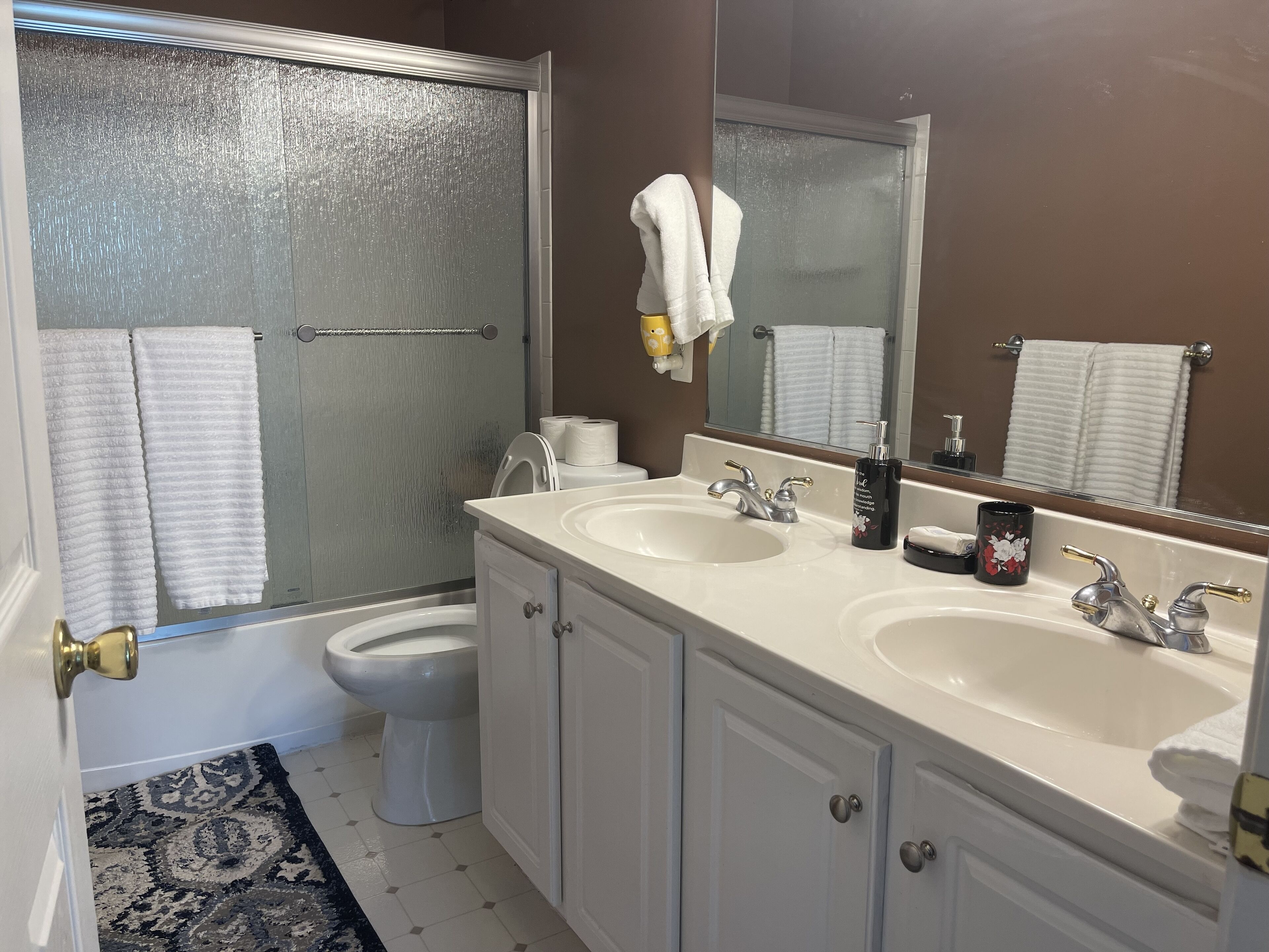 A bathroom with a shower, two sinks, a toilet, and a large mirror.
