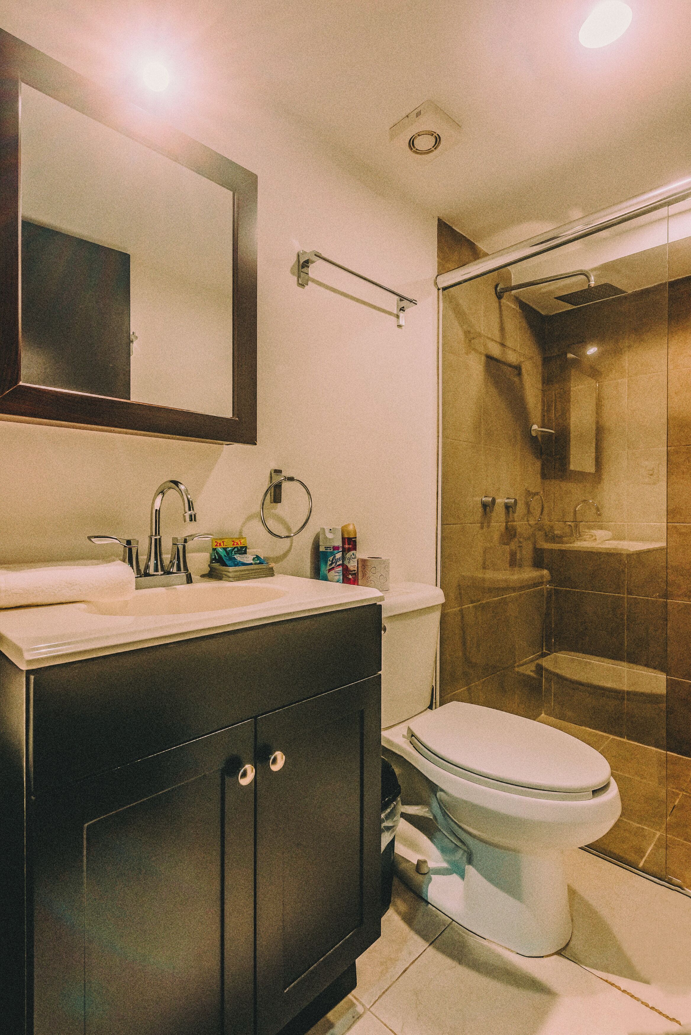 A bathroom with a white sink, dark cabinet, toilet, and a glass shower enclosure.