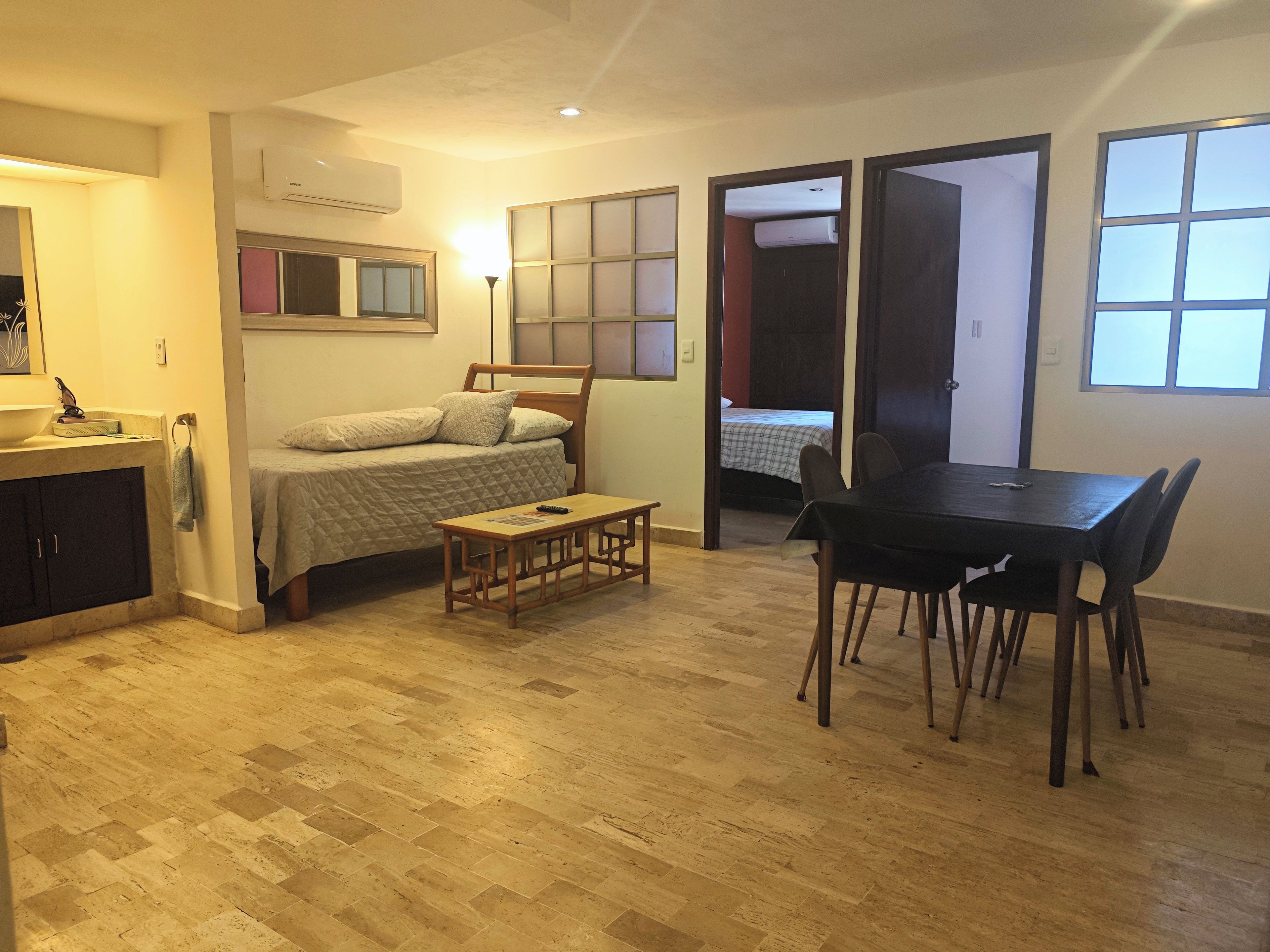 Un espacio habitable compacto con una cama, una mesa de comedor con sillas, una mesita y un espejo.