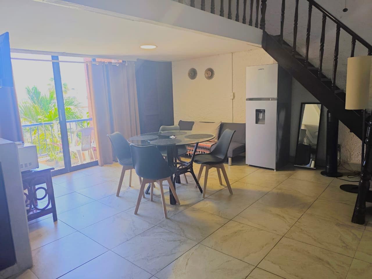 A dining area with a round table and chairs, a refrigerator, and a staircase.