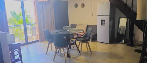 A dining area with a round table and chairs, a refrigerator, and a staircase.