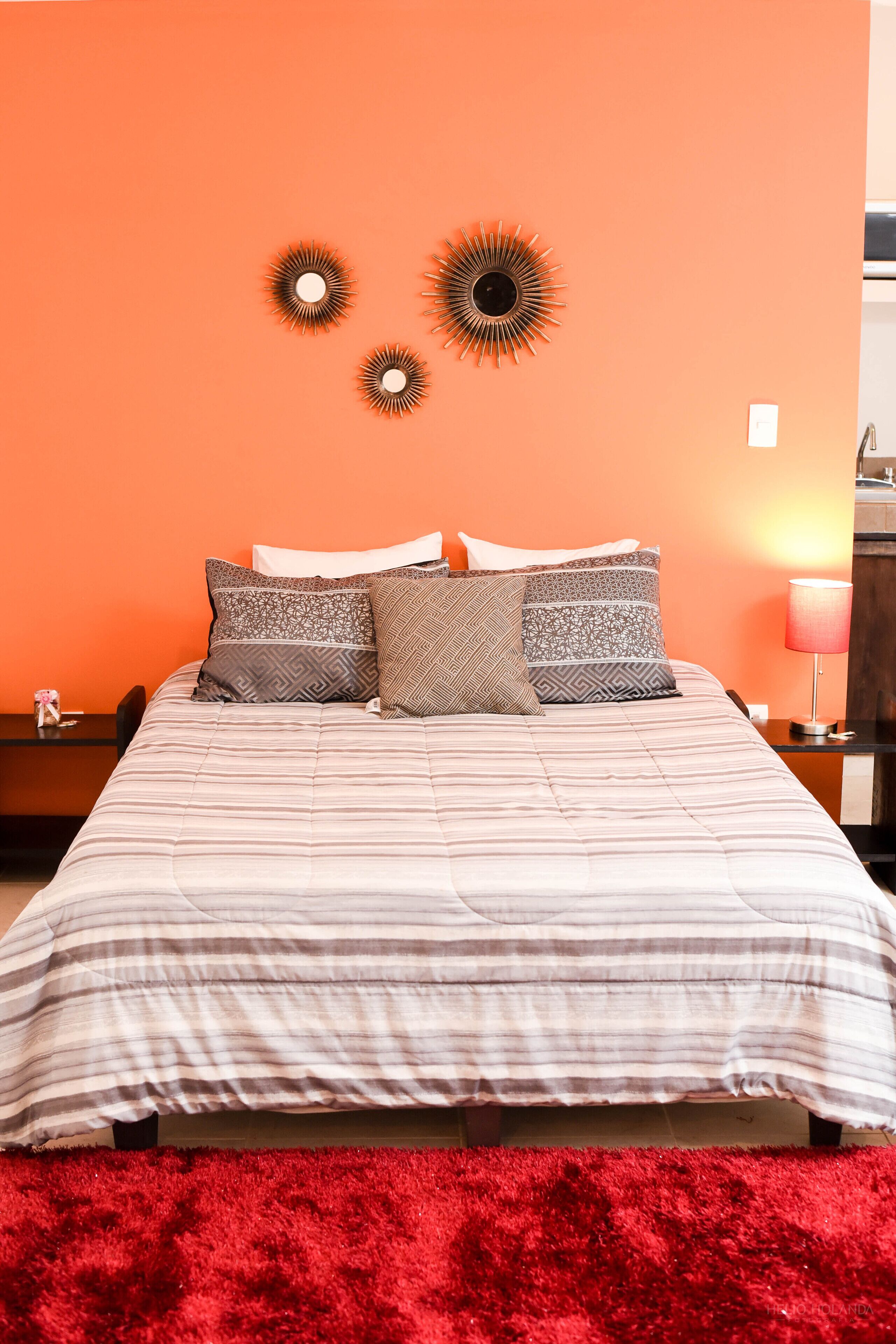 Un lit avec une literie à motifs, un tapis rouge et des éléments de décoration murale.