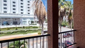 A view from a balcony with a view of the RIU PALACE building, palm trees, and a parking area. - CANCUN SUITES APARTMENTS - HOTEL ZONE (Cancun)