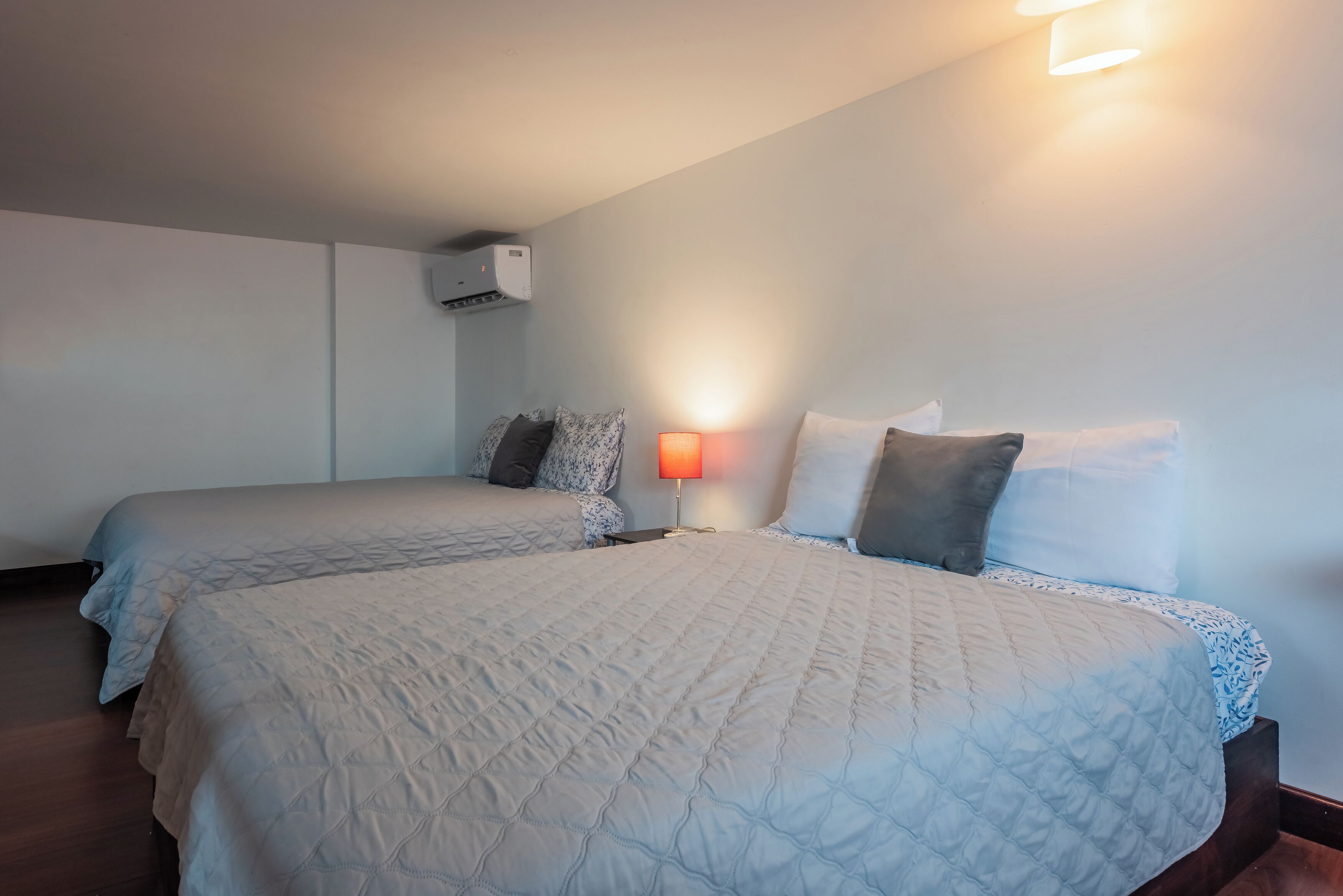 Et hotelværelse med to senge, et sengebord med en lampe og en aircondition på væggen.