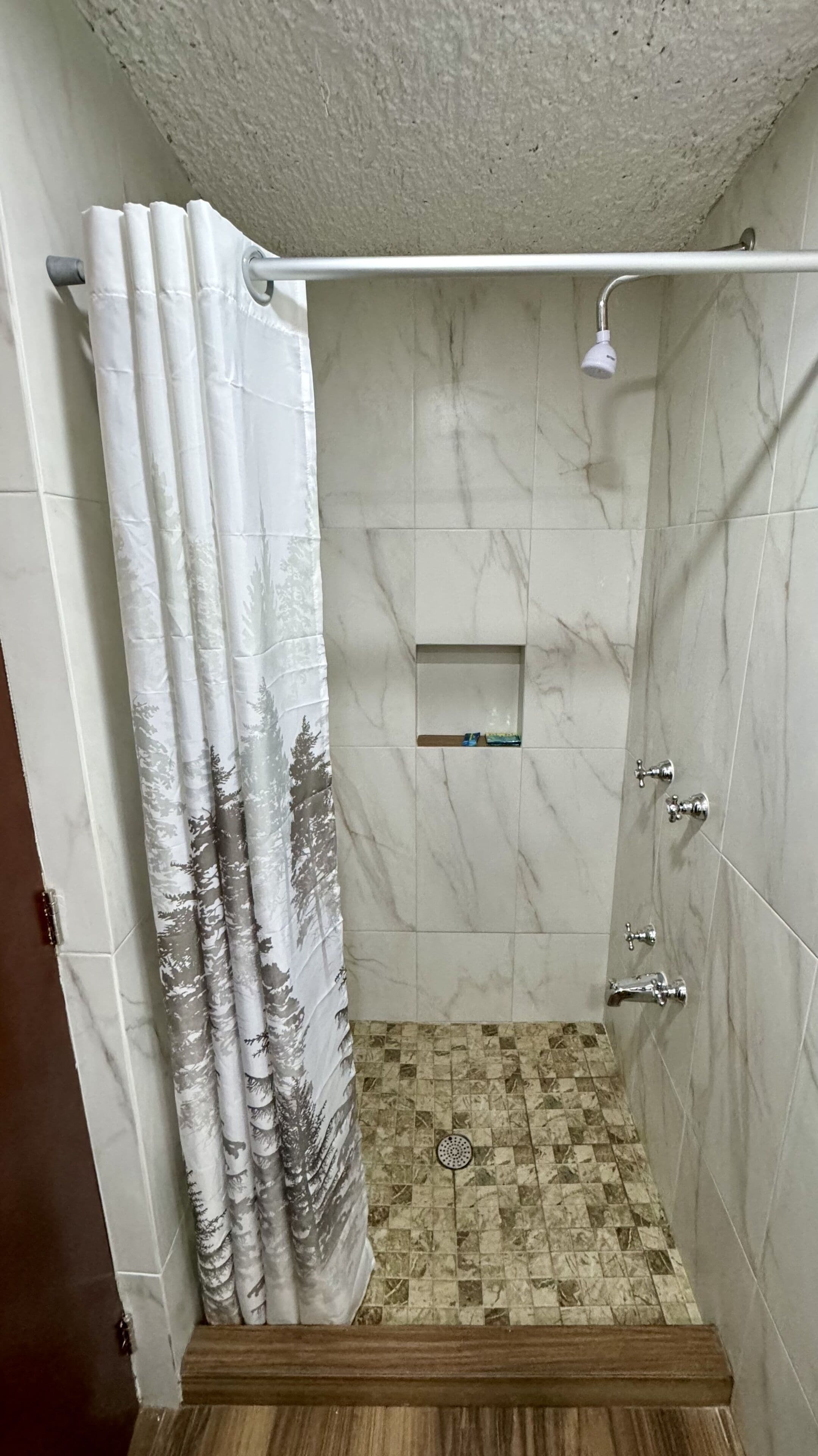 A shower area with a white showerhead, a small shelf, and a patterned shower curtain.