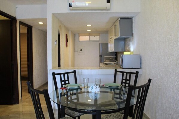 A compact kitchen with a microwave, refrigerator, and a small dining area with a glass table and chairs.